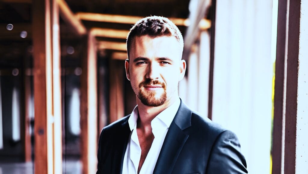 Benedikt Gruber im Business-Outfit lächelnd vor neutralem Hintergrund mit professioneller Körperhaltung