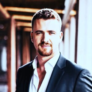 Benedikt Gruber im Business-Outfit lächelnd vor neutralem Hintergrund mit professioneller Körperhaltung